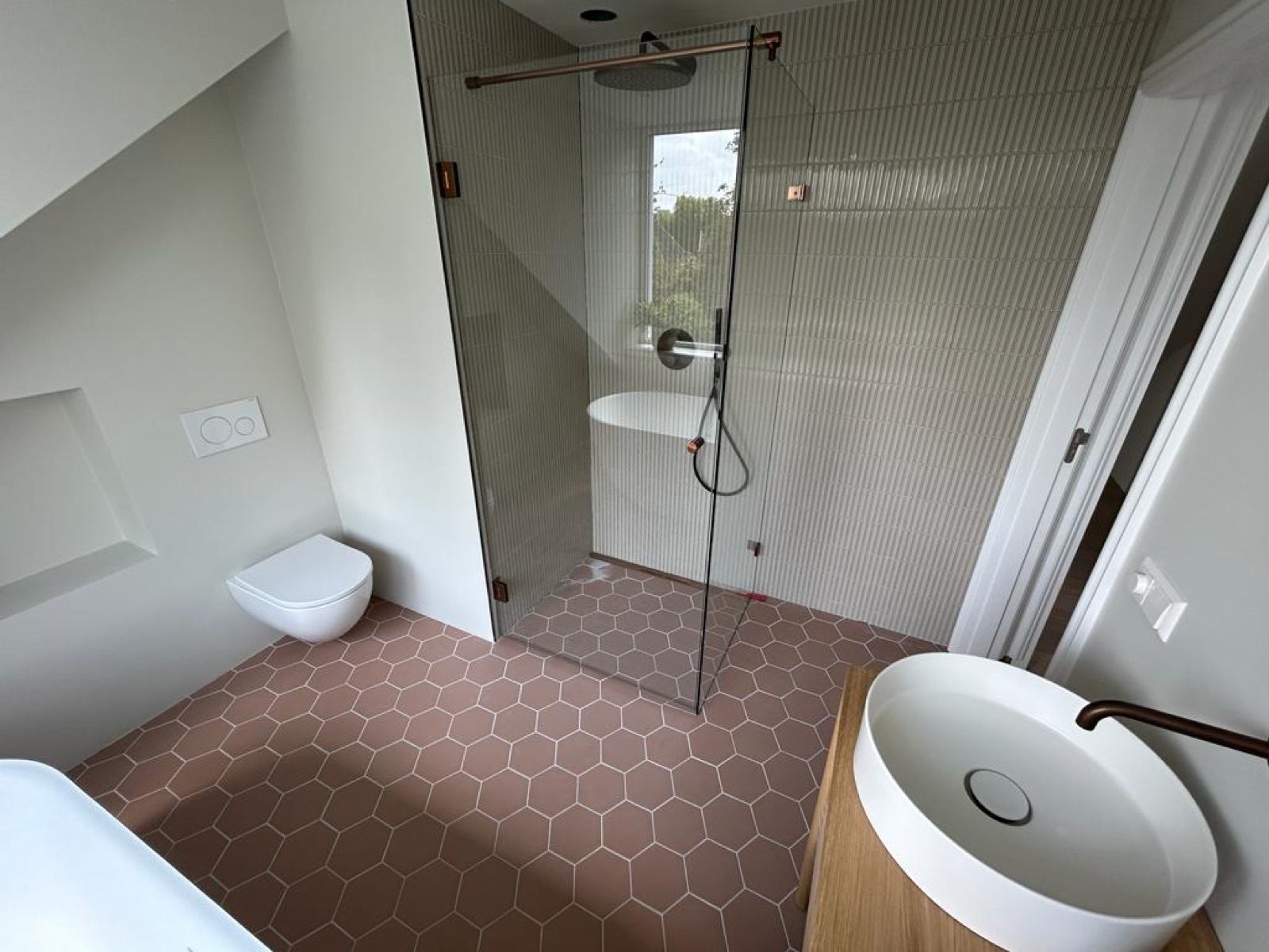 Afgewerkte badkamer met inloopdouche, wandtoilet en zeshoekige vloertegels