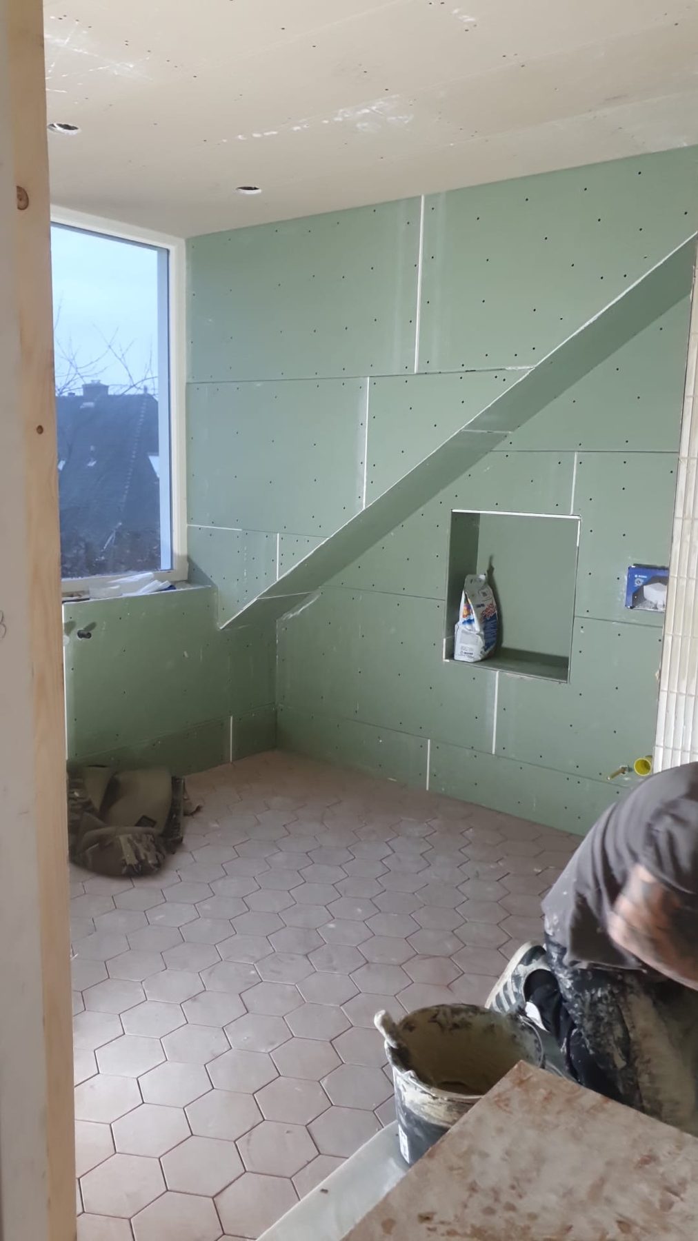 Badkamer in voorbereiding met groene bouwplaten en roze zeshoekige tegelvloer