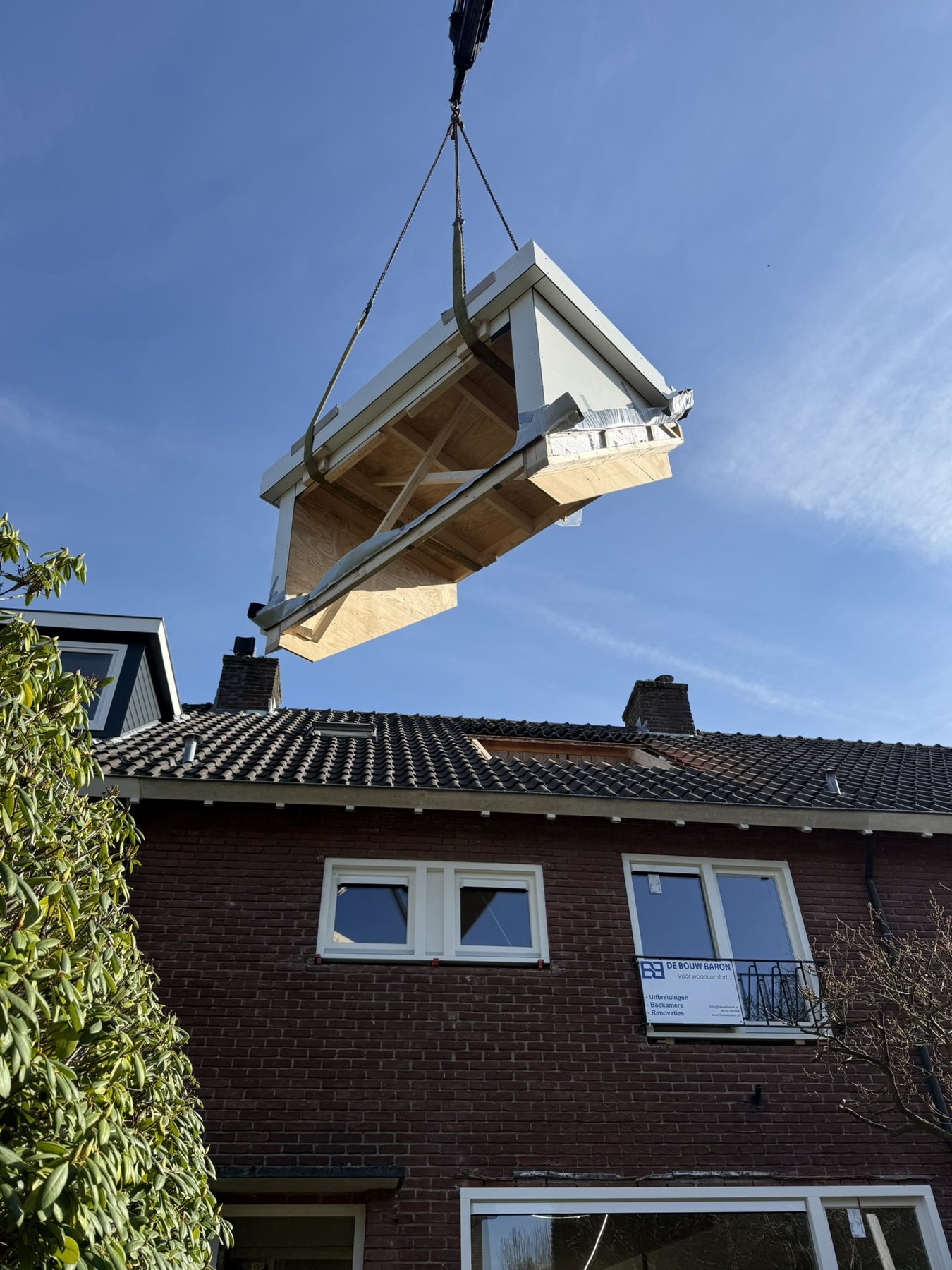 Dakkapel wordt met een kraan boven het dak gehesen